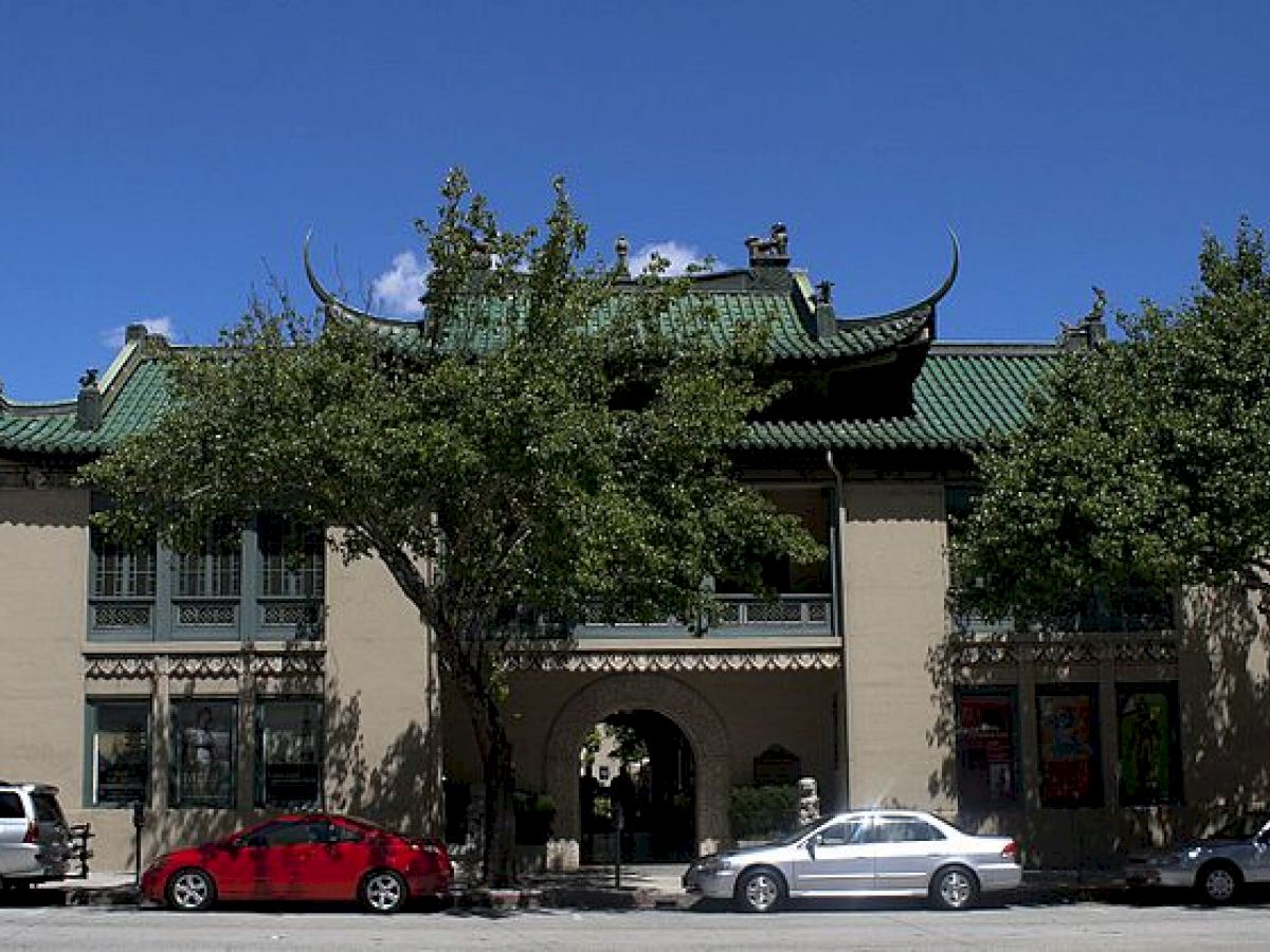 The image shows a building with traditional East Asian architectural elements, including a green tiled roof and ornate decorations, with parked cars in front.