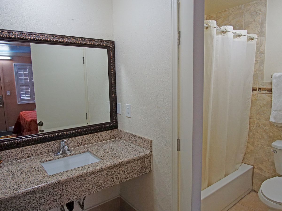 The image shows a bathroom with a sink and mirror on the left, and a toilet and shower with curtain on the right, towels hanging nearby.