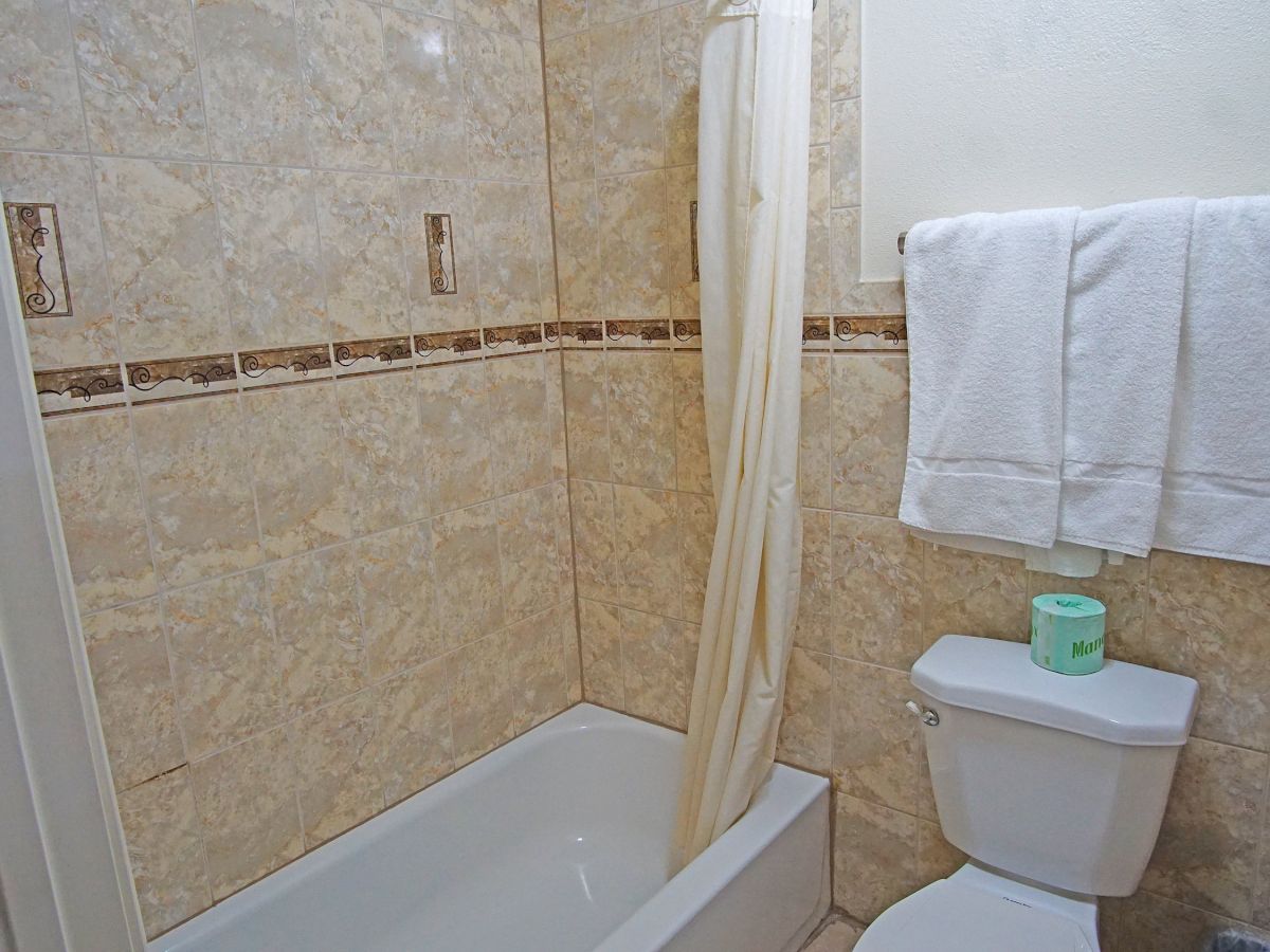 A bathroom with tiled walls, a bathtub with a curtain, a toilet, and white towels hanging on a rack. A green item is on the toilet tank.