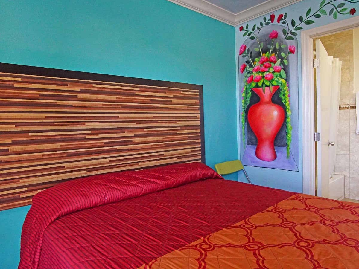 This image shows a brightly painted bedroom with a wooden headboard, red bedspread, and an adjacent bathroom visible through an open door.