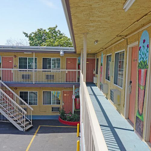 The image shows the exterior of a two-story motel with multiple doors, staircases, and hand-painted murals on the walls.