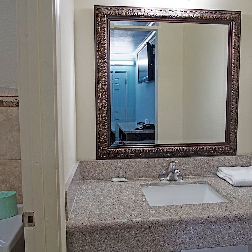 The image shows a bathroom with a mirror above a sink, a towel folded on the counter, a toilet, and towels on a rack.