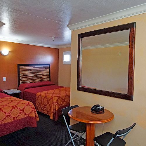 A hotel room with two double beds, a large wall mirror, a small table with a phone, chairs, a microwave, mini-fridge, and a wardrobe.