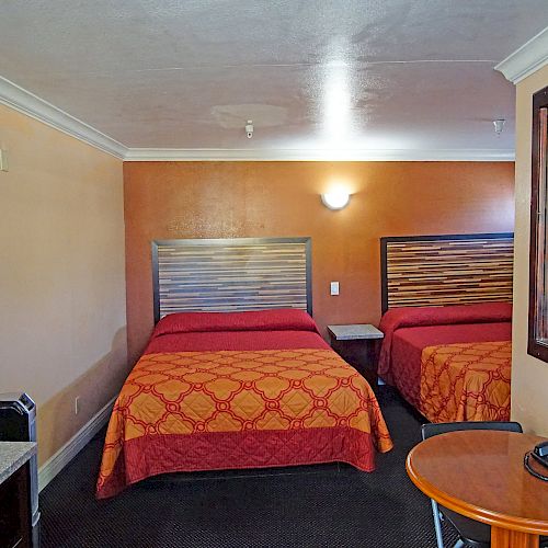 A hotel room with two beds, a wall-mounted TV, a mirror, a round table with a phone, and warm lighting.