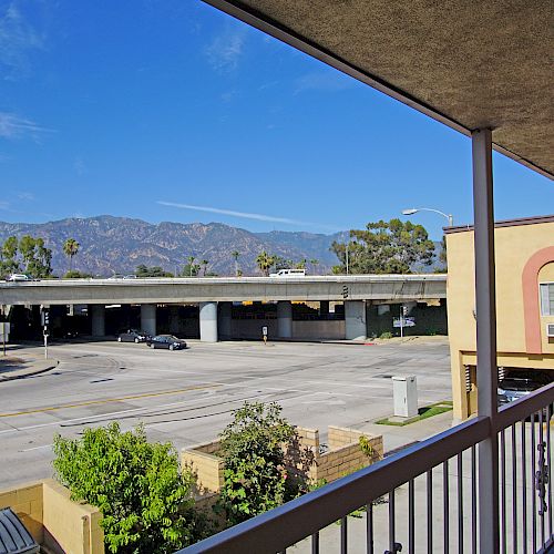 The image shows a view from a building corridor over a road with a bridge, greenery, and mountains in the background under a clear sky ending the sentence.