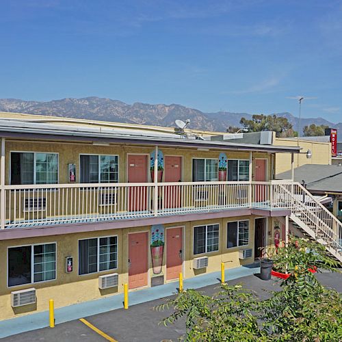 This image shows a motel with two stories, outside stairs, and doors to individual rooms. Mountains and clear blue skies can be seen in the background.