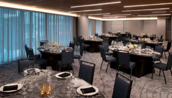 The image shows an elegantly set dining room with round tables covered with silver tablecloths and black napkins, adorned with floral centerpieces.