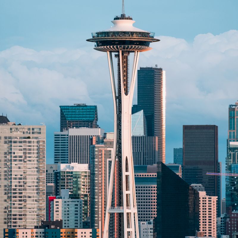 The image shows the Space Needle, a prominent observation tower in Seattle, surrounded by the city's downtown skyscrapers on a clear day.