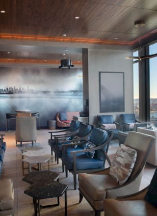 A modern lounge area with plush seating, floor-to-ceiling windows offering a scenic view, a mural on the wall, and elegant lighting.