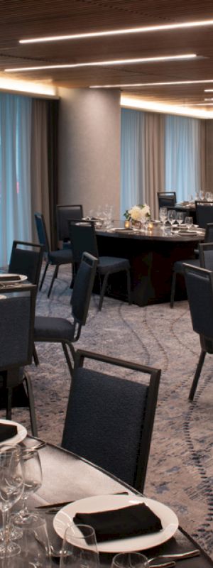 A banquet hall setup with round tables covered in white tablecloths, black napkins, glassware, and floral centerpieces, under modern lighting.