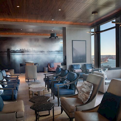 A modern lounge area with comfortable seating, large windows showcasing a waterfront view, and contemporary artwork on the wall.