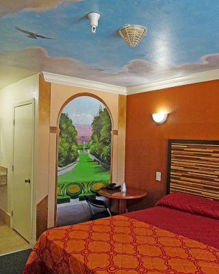 This image depicts a vibrant hotel room with colorful murals, a red bedspread, a small table, and a view into the bathroom with a mirror and sink.