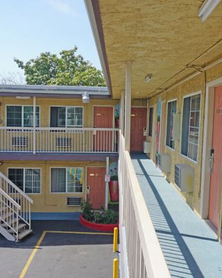 This image depicts the exterior of a two-story motel with cream-colored walls, peach doors, and painted decorations, featuring an outdoor staircase.