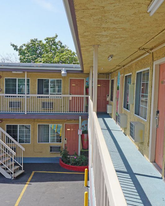 This image depicts the exterior of a two-story motel with cream-colored walls, peach doors, and painted decorations, featuring an outdoor staircase.